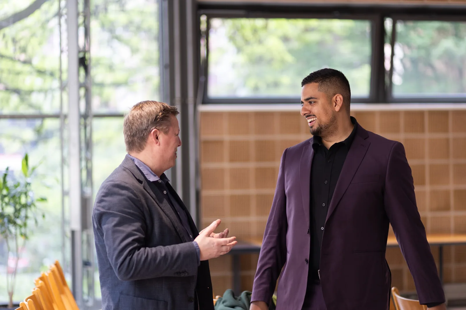 Mark Kashef in a purple suit, smiling mid-conversation with an event guest by the windows