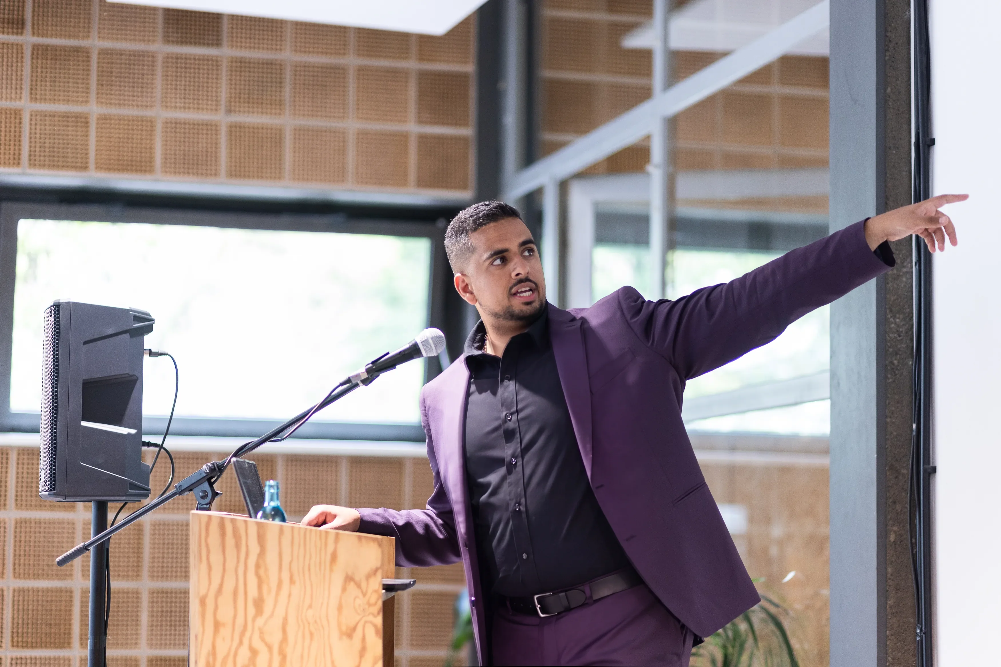 Mark Kashef in a purple suit, pointing across the stage against giant industrial windows