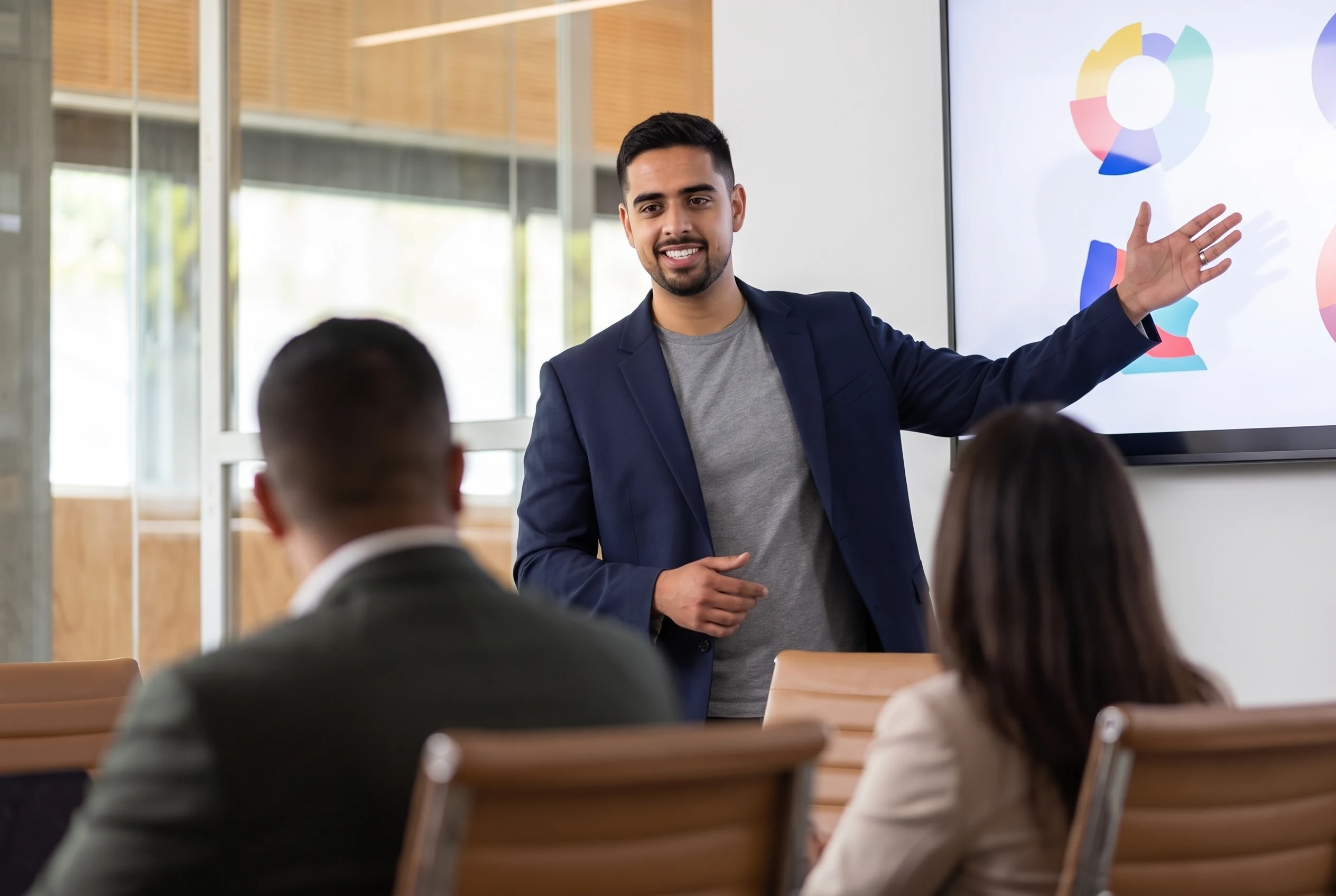 Mark presenting charts on a wall screen to a small team in a bright boardroom
